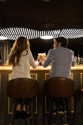 Rückansicht eines Paares, das in einer Bar mit Biergläsern anstößt - VABF01708