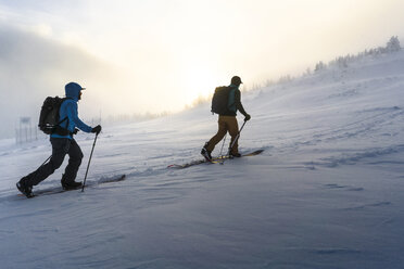 Männliche Freunde beim Spaziergang auf einem verschneiten Feld bei nebligem Wetter - CAVF54088