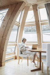 Woman using mobile phone while sitting on chair at home - CAVF54093