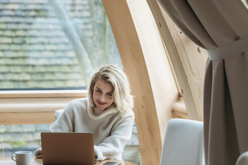 Frau benutzt einen Laptop, während sie zu Hause am Fenster sitzt - CAVF54095