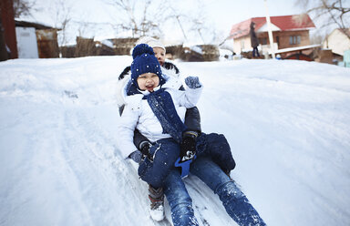 Cheerful mother and daughter tobogganing on snowy field - CAVF54098