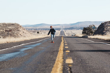 Full length of man skateboarding on road amidst field against clear sky - CAVF54103