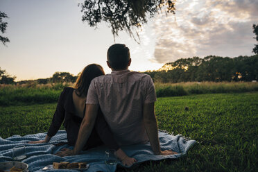 Rückansicht eines Paares, das sich auf einer Decke gegen den Himmel im Park bei Sonnenuntergang entspannt - CAVF54141
