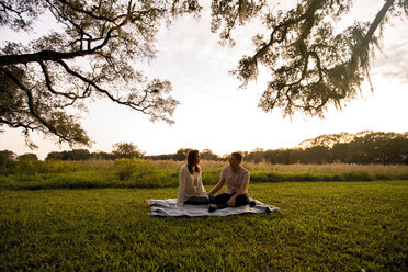 Couple talking while sitting on blanket at park during sunset - CAVF54145