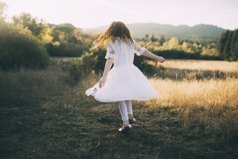 Verspieltes Mädchen im weißen Kleid beim Spinning im Park in voller Länge - CAVF54157