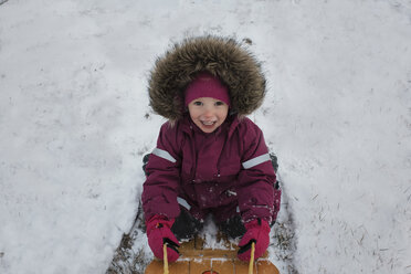 Hochformatiges Porträt eines Mädchens beim Rodeln auf einem verschneiten Feld - CAVF54185
