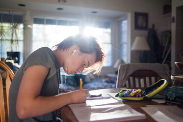 Side view of teenage girl listening music while writing homework at home - CAVF54220