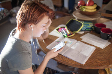 Side view of teenage girl using mobile phone while sitting on chair at home - CAVF54222