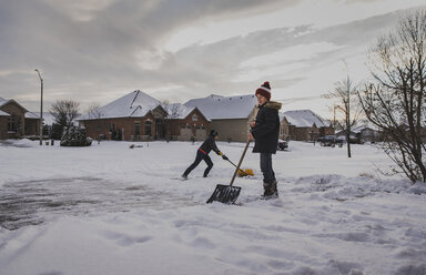 Brüder schaufeln Schnee auf der Straße vor den Häusern - CAVF54234