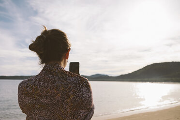 Rückansicht einer Frau, die mit ihrem Mobiltelefon am Strand fotografiert, gegen einen bewölkten Himmel - CAVF54236