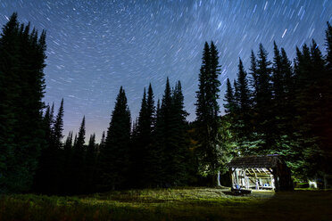 Illuminated shed by trees against star trails - CAVF54258