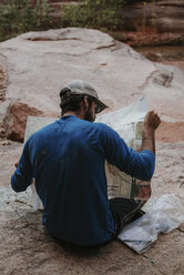 Rückansicht eines Mannes, der sitzend im Grand Canyon National Park eine Karte liest - CAVF54264