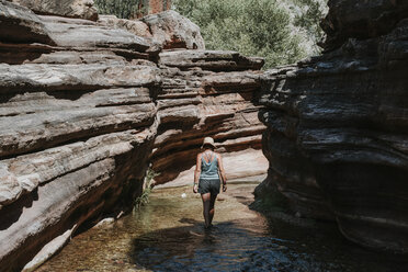 Rückansicht einer Frau, die im Fluss inmitten von Felsformationen im Grand Canyon National Park spazieren geht - CAVF54265