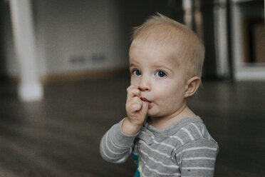 Portrait of baby boy thumb sucking while sitting on floor at home - CAVF54271