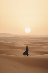Rückansicht einer Frau, die eine Laterne hält, während sie in der Wüste Sahara vor dem Himmel bei Sonnenuntergang steht - CAVF54289