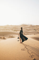 Side view of woman holding lantern while standing at Sahara Desert against clear sky during sunset - CAVF54292
