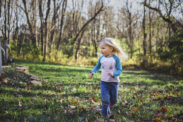 Girl running on grassy field at park during autumn - CAVF54300