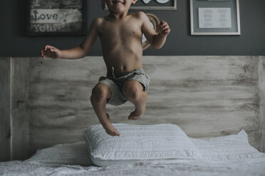 Verspielter Junge ohne Hemd, der zu Hause auf dem Bett springt - CAVF54314