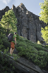 Low angle view of man with backpack standing on mountain against sky - CAVF54320