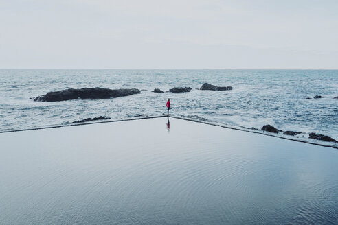 Mid distance view of woman standing amidst swimming pool and sea against clear sky - CAVF54333