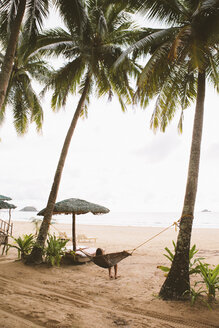 Rear view of woman relaxing on hammock at beach against sky - CAVF54341