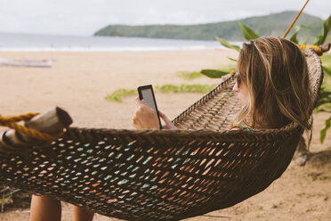 Frau benutzt Tablet-Computer und entspannt sich in der Hängematte am Strand - CAVF54342