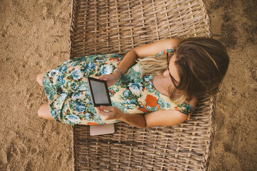 High angle view of woman using tablet computer while relaxing on hammock at beach - CAVF54343