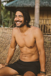 Mann ohne Hemd schaut weg, während er sich auf einer Hängematte am Strand entspannt - CAVF54344