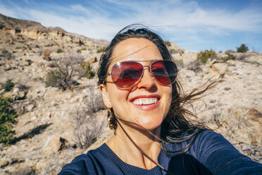 Porträt einer fröhlichen Frau mit Sonnenbrille in der Wüste - CAVF54362