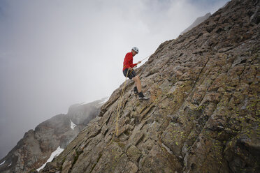 Seitenansicht eines Wanderers, der ein Seil benutzt, während er gegen die Wolken auf Felsformationen klettert - CAVF54365