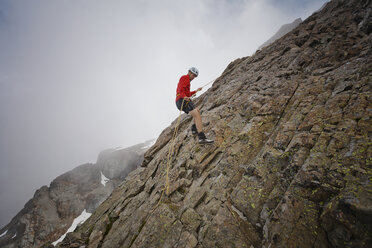 Side view of hiker using rope while climbing rock formations against clouds - CAVF54365