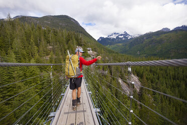 Rückansicht eines Wanderers mit Rucksack beim Überqueren eines Stegs inmitten des Waldes - CAVF54367