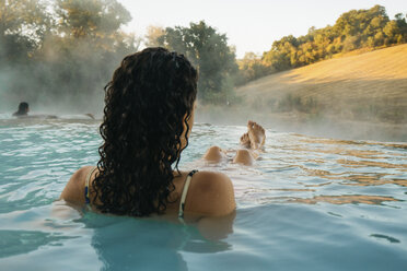 Rear view of woman relaxing in thermal pool - CAVF54385