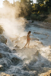 High angle view of woman walking on rock in steam emitting thermal pool - CAVF54386