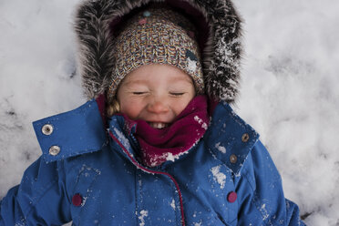 High angle view of smiling girl with eyes closed lying on snow covered field - CAVF54399