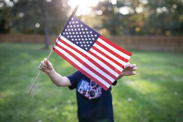 Junge zeigt amerikanische Flagge, während er auf einem Feld im Hof steht - CAVF54439