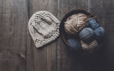 Draufsicht auf eine Strickmütze mit Wollknäueln in einer Schale auf dem Tisch - CAVF54445