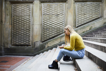 Full length of woman using smart phone while sitting on steps at park - CAVF54478