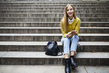 Portrait of smiling young woman sitting on steps at park - CAVF54479