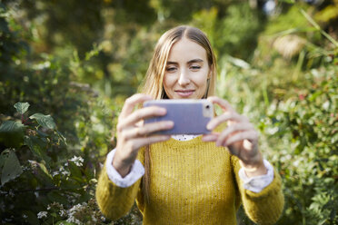 Junge Frau beim Fotografieren inmitten von Pflanzen stehend - CAVF54484