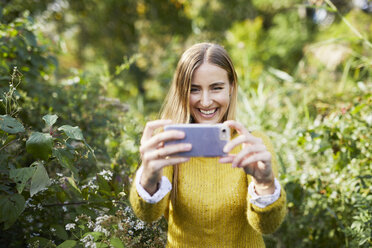 Cheerful Young woman photographing while standing amidst plants - CAVF54485