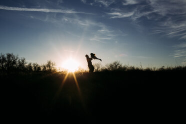 Silhouette Vater hebt Tochter beim Spielen mit ihr auf Feld gegen Himmel bei Sonnenuntergang - CAVF54489