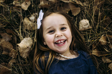 Overhead portrait of cute cheerful girl lying on field at park during autumn - CAVF54491