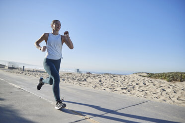 Frau in voller Länge beim Joggen auf der Straße am Strand gegen den klaren Himmel - CAVF54494