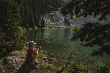 Father and son fishing in lake against mountains at forest - CAVF54500