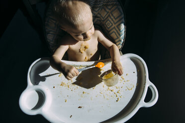 High angle view of shirtless baby boy eating food while sitting on high chair at home - CAVF54515