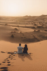 Rückansicht von Freunden, die auf Sand in der Sahara-Wüste sitzen, gegen den Himmel bei Sonnenuntergang - CAVF54519