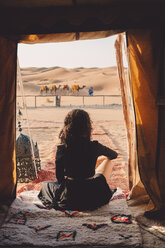 Rear view of woman sitting on blanket at Sahara Desert seen through tent - CAVF54521