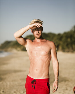 Porträt eines am Strand stehenden Mannes ohne Hemd vor dem Himmel - CAVF54525