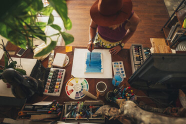 Hochformatige Ansicht eines Malers, der zu Hause stehend auf einem Tisch malt - CAVF54533